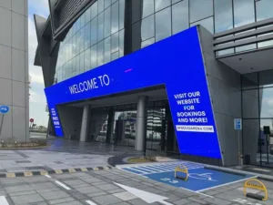 A large LED screen at a building entrance, showcasing a blue display with friendly lettering